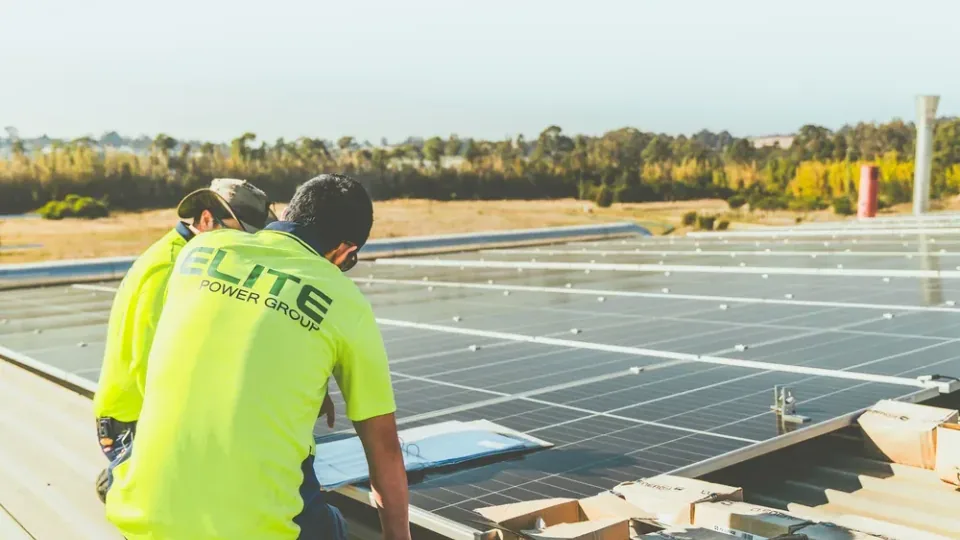 Técnicos instalando painéis solares em telhado comercial