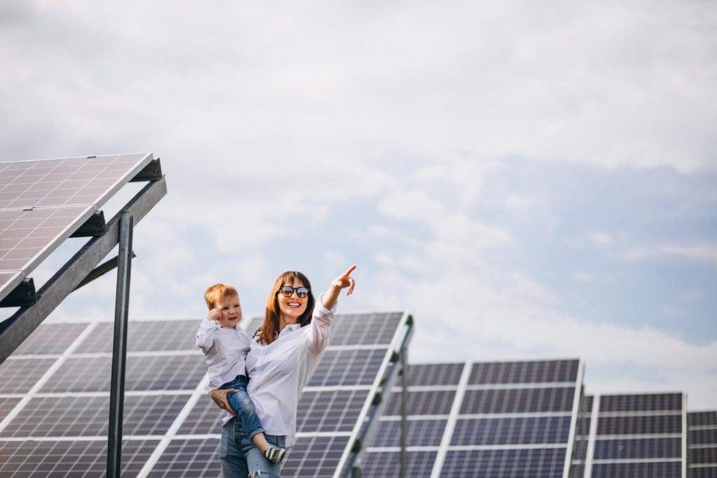 Mulher com filho no colo perto de painéis solares em uma Fazenda Solar